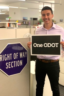 Right of Way employee holding a sign that reads One ODOT