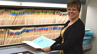 Employee standing in front a shelf of file folders.
