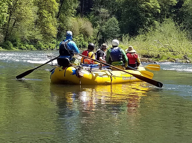 People in a rubber boat holding paddles and floating down a river
